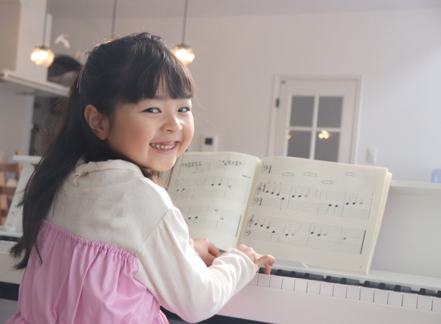 ピアノの前に笑顔で座る女の子